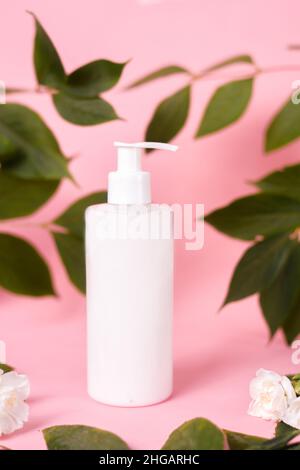 Cosmetics, cream with dispenser, lotion on a pink background. White bottle on a background of leaves and flowers. Natural cosmetic Stock Photo