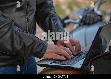 Close up of unrecognizable man using a laptop while traveling with his motorcycle. Stock Photo