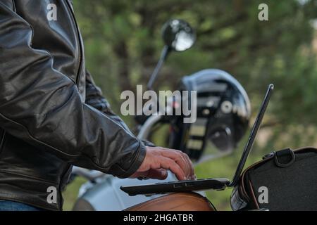 Side view of an unrecognizable man using a laptop while traveling with his motorcycle. Stock Photo