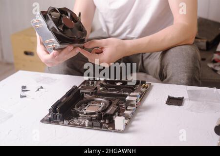 Computer technician installs cooling system of computer. Engineer repairing computer (pc) board. Technician plug in electronic parts on motherboard.A Stock Photo