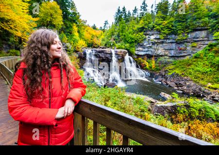 Young woman on wooden boardwalk deck overlook railing at Blackwater Falls waterfall state park in West Virginia autumn fall season looking at view hap Stock Photo