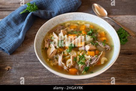 Homemade chicken soup with root vegetable and noodles served on a plate isolated on wooden table from above with copy space Stock Photo