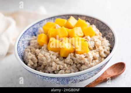 Oatmeal porridge in bowl with mango cut in cubes. Healthy breakfast for weight loss and wellness. Stock Photo