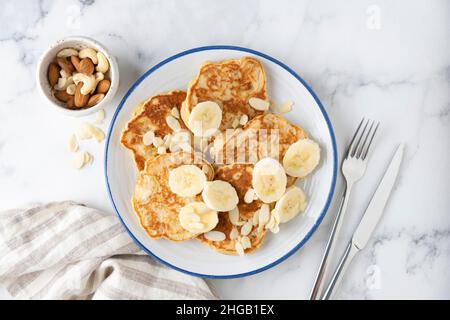 Banana protein pancakes with almond flakes on plate, white marble background, top view Stock Photo
