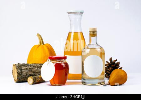 Homemade fruit juice, jam and alcohol. Transparent glass bottles and jar, pumpkin, pear, branches, fruits and logs on background. Natural production c Stock Photo