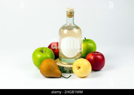 Homemade natural alcohol production concept. Transparent glass bottle on cross cut wooden logs, pear and various color apples isolated on white backgr Stock Photo