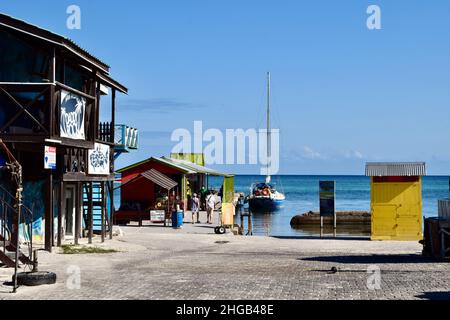 Tourists walking to the ocean ferry terminal in San Pedro, Belize with a docked sailboat and a restaurant to the left of the image. Stock Photo