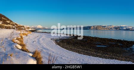 The View at the island of Senja and the fjord in the Atlantic Ocean with a snowy field in the polar area and mountains covered in snow near Tromso Nor Stock Photo