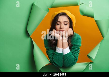 Young white upset sad woman peeking out hole isolated on green background Stock Photo