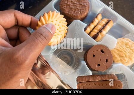 Adult Asian male picking a biscuit from biscuit collection box Stock Photo