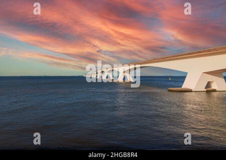 Zeeland Bridge - long white bridge over the river, beautiful blue sky with dynamic clouds. Long time, calm water of the Oosterschelde. Sunset. Stock Photo