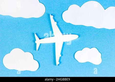 White plane model on light sky blue background with paper clouds top view flat lay. Stock Photo