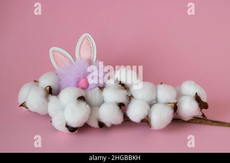 Beautiful white cotton flowers and a small fluffy lilac toy rabbit on a pink background. Easter Concept. Stock Photo
