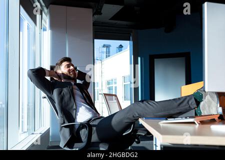Satisfied businessman, happy and resting, man threw his feet on the table, and dreams of successful projects Stock Photo