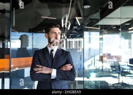 Successful business owner in a modern office, man with his hands folded on the cross, looks away and smiles Stock Photo
