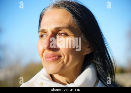 Profile side view portrait of attractive cheerful dreamy grey-haired middle-aged woman relaxing outdoors during sunny day Stock Photo