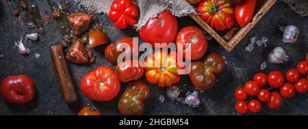 Kitchen panorama, banner - colorful ripe organic heirloom varieties tomatoes with knife and wooden box on a dark table background. The concept of harv Stock Photo