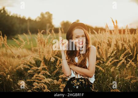 Beauty Girl Outdoors enjoying nature. Pretty Teenage Model in hat running on the Spring Field, Sun Light.  Romantic young blonde girl in a wheat field Stock Photo