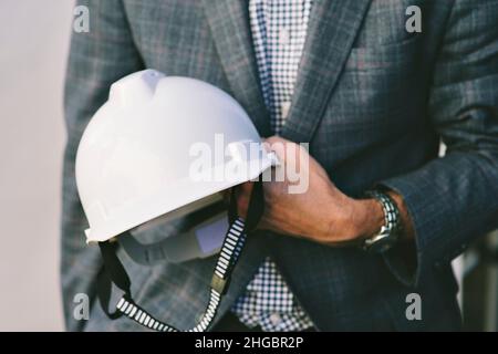 Businessman holds a white hard hat while wearing a business suit Stock Photo