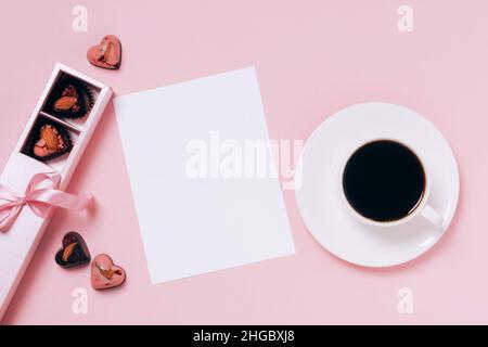Chocolate candies hearts festive box, cup of coffee, blank sheet of paper pink background. Concept Valentine's Day Stock Photo
