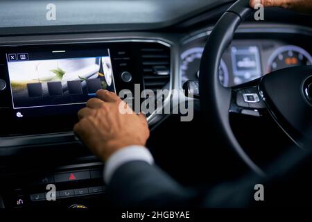 Close up of man in suit tapping with finger on multimedia screen of dashboard while sitting in side luxury car. Male customer testing auto at modern showroom. Stock Photo