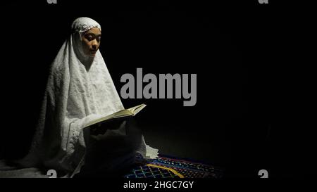 Muslim Woman Reading Quran in a Dark Room Stock Photo