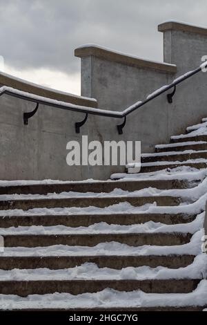 Stone concrete snow-covered stairs with footprints in the city in winter. Stairs with ice and snow Stock Photo