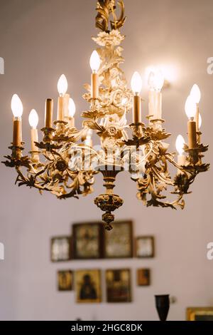 Gold chandelier with bulbs hanging in the church against the background of the wall with icons Stock Photo