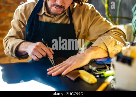 hobby became a small business leather man in apron is making a leather wallet and shooes in studio Stock Photo