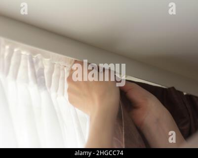 Hands of a young man hang curtains on the ledge on the window Stock Photo