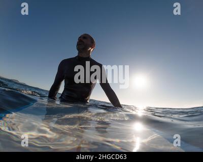 Caucasian surfer sitting on his surfboard in the water waiting for waves