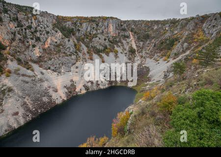 Blue lake, a large sinkhole close to more known Red lake at the edge of village of Imotski in southern Croatia on a gray day. Stock Photo