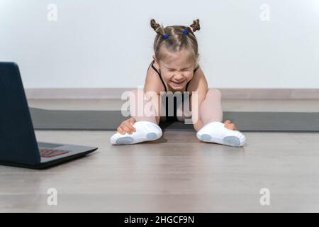 remote training of a child ballerina online during quarantine. girl doing stretching, training foot eversion. Stock Photo