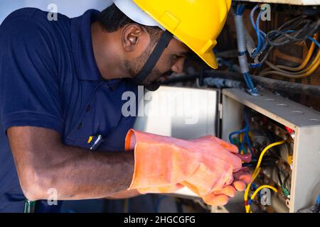 Focus on hand, young electrical engineer with protective workware repairing or connecting wires by using screw driver at workplace - Concept of hard Stock Photo
