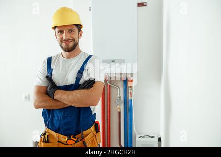 Smiling technician servicing the house heating system looking at camera while standing with arms crossed Stock Photo