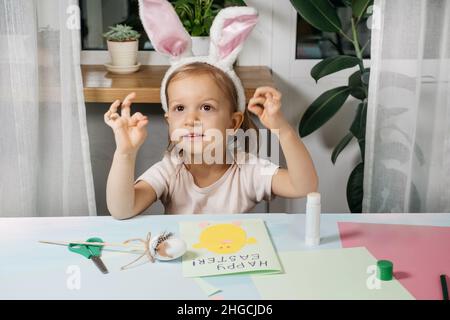 Child making Easter egg gift card with a bunny from paper at home. Handmade. Project of children's creativity, handicrafts, crafts for kid, toddler. Stock Photo