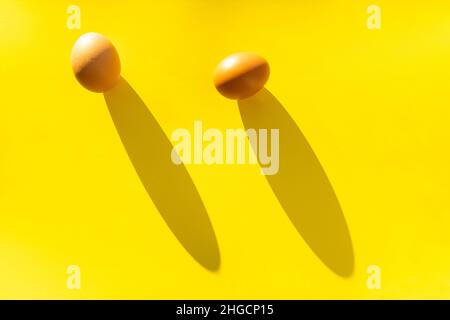 Two brown farm eggs on a yellow background in bright light, a concept of minimalism. Stock Photo