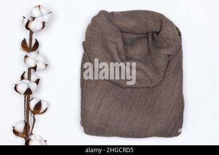 Warm brown wool sweater with white cotton flower sprig on white background top view. Cozy winter wear Stock Photo