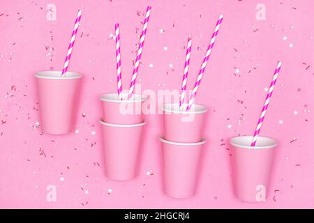 Pink paper cups with striped drinking straws and candy sprinkles on pink background. Girly party, sweet beverage concept Stock Photo