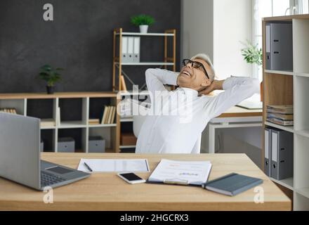 Happy satisfied senior businessman relaxing at office desk after his working day Stock Photo