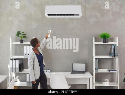 Black woman uses a remote control to switch on the air conditioner in the office Stock Photo