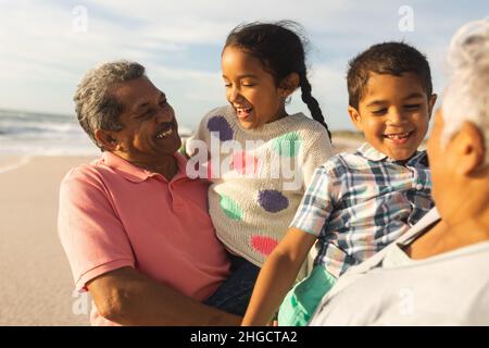 Smiling multiracial grandparents carrying grandchildren enjoying weekend together at sunny beach Stock Photo