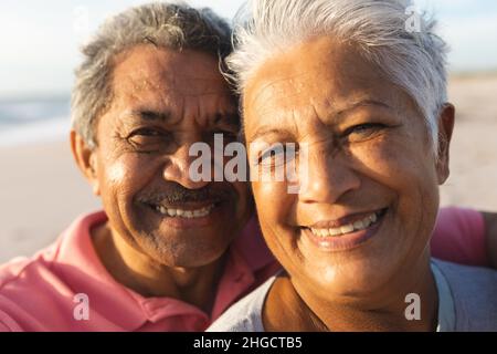 Close-up portrait of smiling multiracial senior couple with white hair enjoying sunset at beach Stock Photo