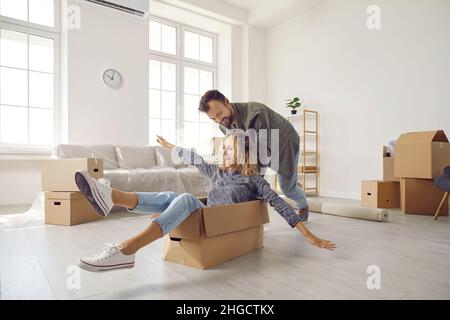 Happy young married couple having fun using cardboard boxes in new home on moving day. Stock Photo