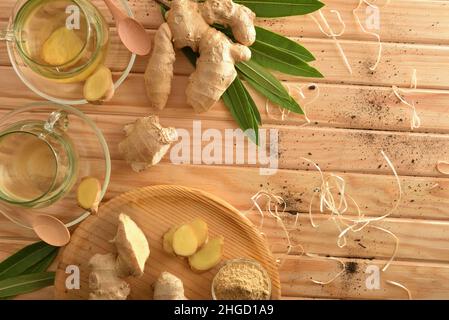Organic ginger infusions on wooden table in the countryside with root ginger and sliced portions, ginger powder in container, straw leaves and soil. T Stock Photo