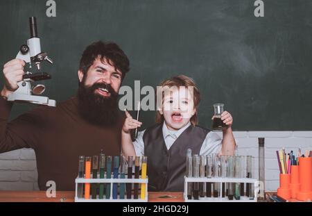 Little kid scientist earning chemistry in school lab. Biology experiments with microscope. Man teaches child. Daddy and his little son ready for Stock Photo