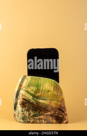 Smartphone in a stand made of stabilized maple wood on a yellow background. Copy space Stock Photo