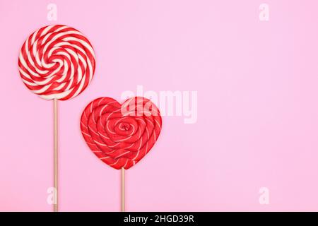 Round two-tone candy and a red heart-shaped lollipop on a pink background. Stock Photo