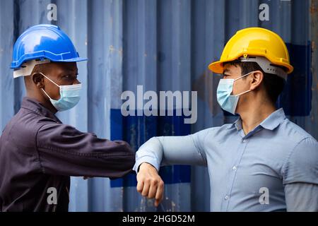 african engineer and caucasian businessman wearing face mask to protect from covid or coronavirus in cargo warehouse at the dock have greeting and tou Stock Photo