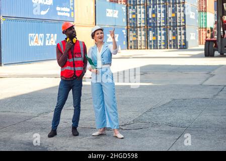 Businesswoman and engineer talking and checking loading Containers box from Cargo freight ship for import export. shipping in docks. Stock Photo